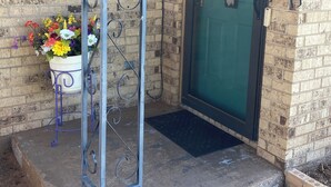 Un edificio de ladrillo con una puerta verde, un portón metálico y una maceta en el suelo.