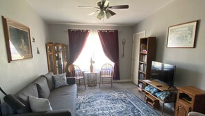 Una sala de estar con sofá, sillas, televisión, estantería y ventilador de techo.
