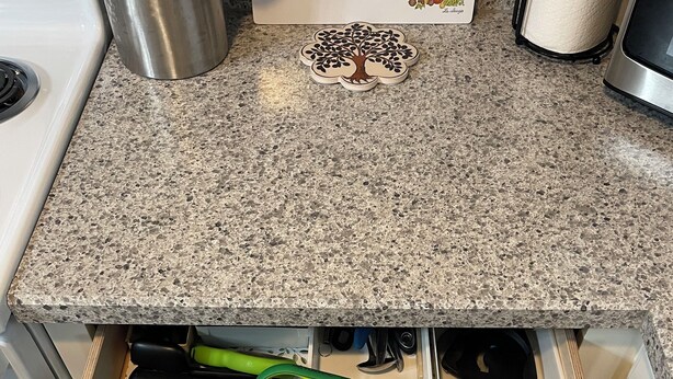 Una encimera de cocina con cubierta de granito, un reposa ollas de acero inoxidable y una pegatina decorativa con forma de árbol.
