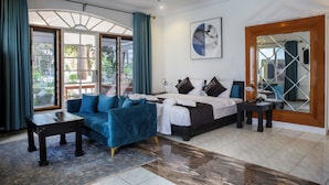 A modern hotel room with a large bed, a blue sofa, a small table, and a large window with curtains. - Coconut Residence & Spa (Serrekunda)