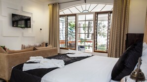 A hotel room with a large bed, a sofa, a TV mounted on the wall, and a window with curtains. - Coconut Residence & Spa (Serrekunda)