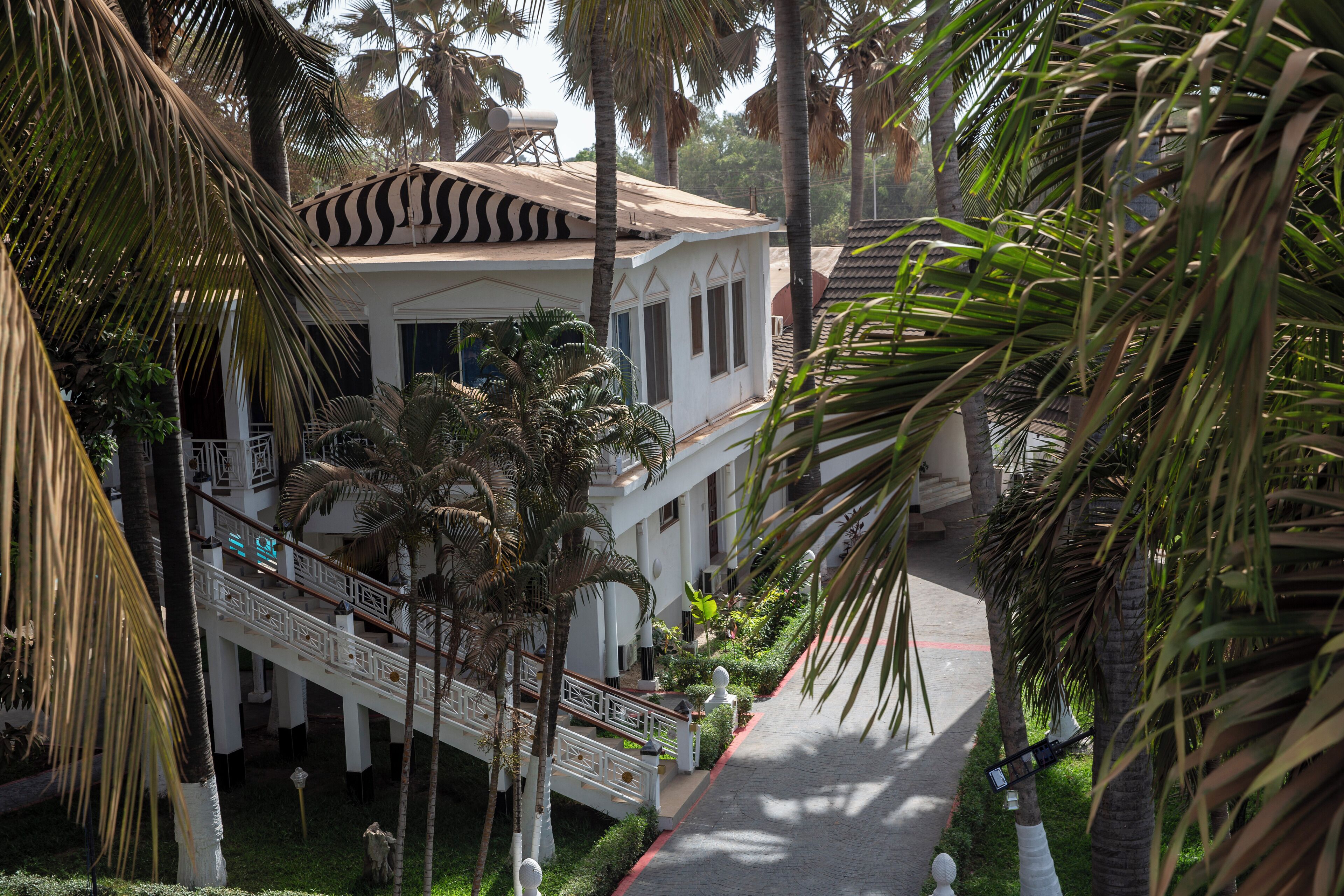 A white building with a zebra-striped awning, surrounded by palm trees and a pathway.