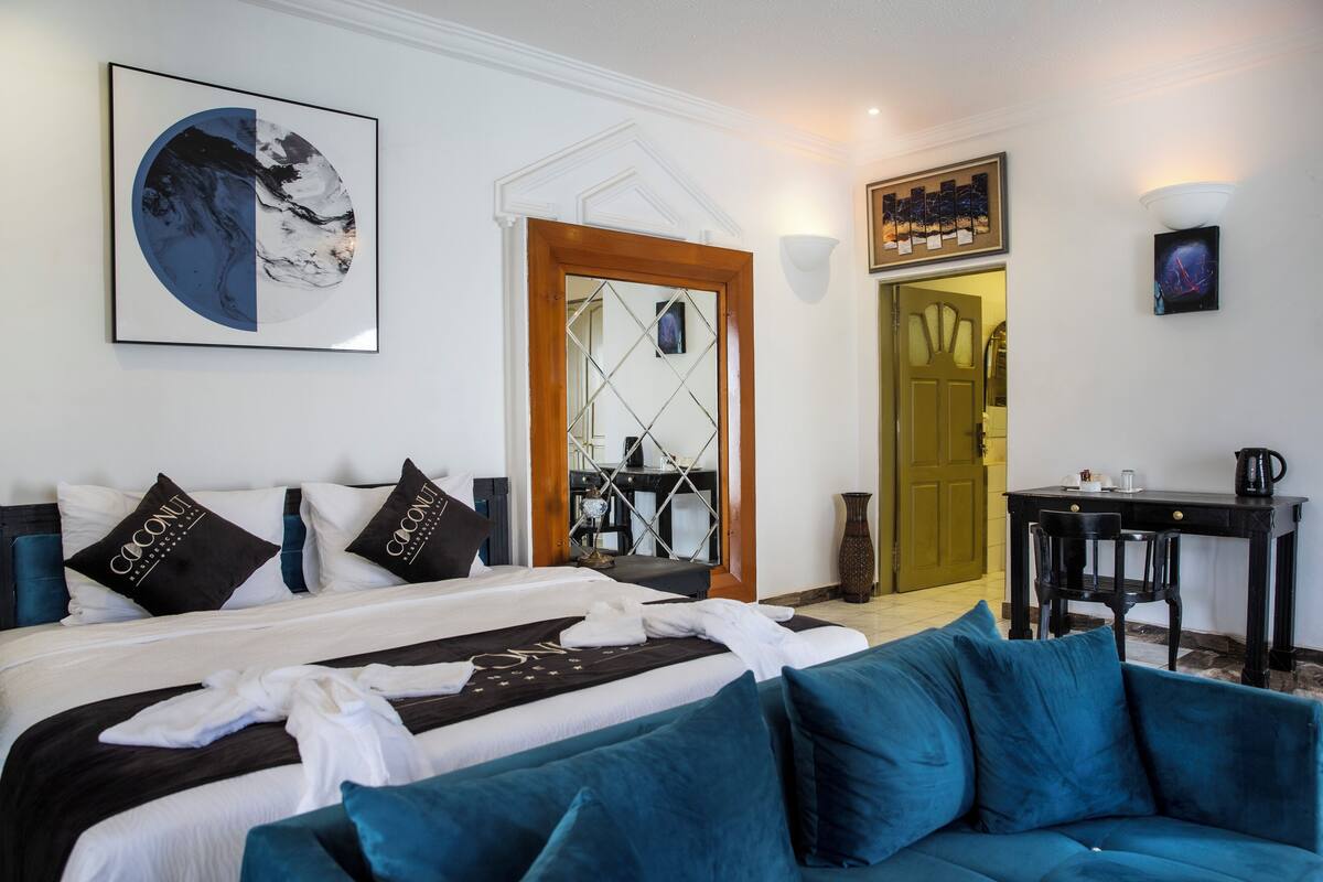 Quarto de hotel com uma cama, um sofá azul, uma mesa de centro e uma escrivaninha com uma cadeira.