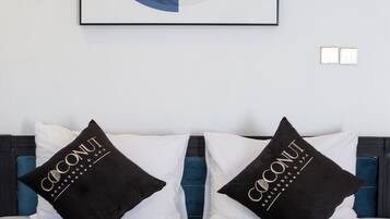 Una habitación de hotel con una cama, dos almohadas negras con la marca 'Coconut', un edredón blanco y una obra de arte enmarcada sobre la cama.