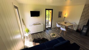 A cozy living room with a sofa, a small table with a bowl of fruit, a white cabinet with a branch, and a TV mounted on the wall. - MoreView Kopice directly on the Szczecin Lagoon (Stepnica)