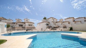 Una piscina con una línea de agua azul cristalina, rodeada de edificios blancos con techos de tejas y balcones.