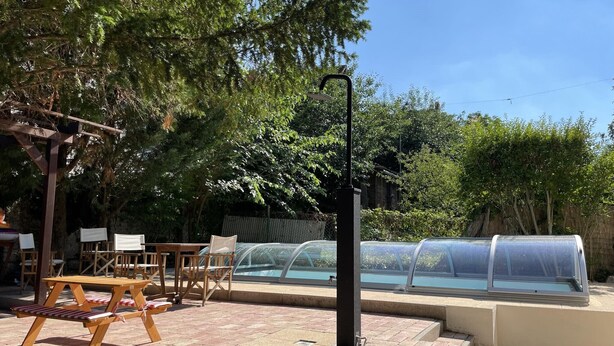 A patio area with a wooden table and chairs, a small pool with a glass enclosure, and a pergola with climbing plants. - See Haus - Podmaniczky (Balatonfoldvar)