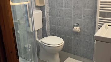 A bathroom with a toilet, a shower enclosure, a sink, and a window.