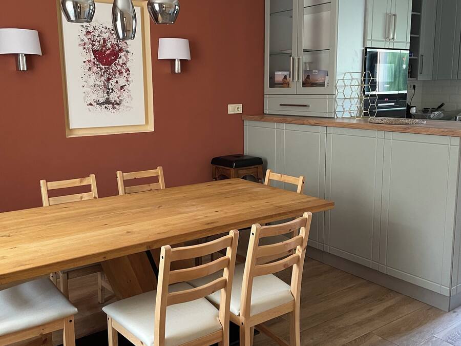 Un comedor con una mesa y sillas de madera, una cocina al fondo y lámparas colgantes en el techo.