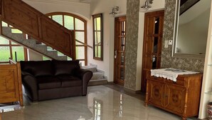 A spacious living area with a high ceiling, a wooden staircase, a large window, and a wooden cabinet with a mirror. - See Haus - Podmaniczky (Balatonfoldvar)