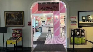 An entrance to a themed shop with a pink and white striped floor, a sign reading "The Ice Cream Shopper," and a security warning sign.