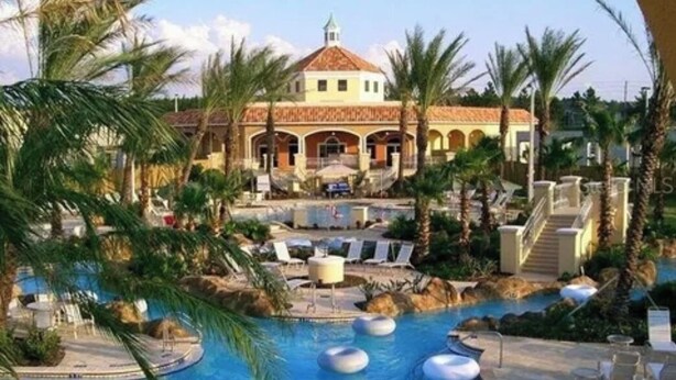 Een resort met een centraal gelegen zwembad, palmbomen en een gebouw met een betegeld dak.