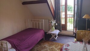 A bedroom with a single bed, a radiator, a window with curtains, a small table with a vase, and a lamp. - Belle Chambre Lumineuse et Chaleureuse au Calme (Chennevières-sur-Marne)