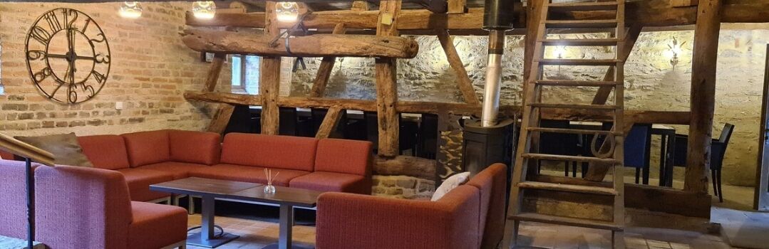 Un interior rústico con techo de madera, pared de piedra, un sofá rojo y una mesa.