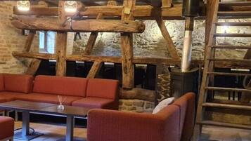 Un interior rústico con techo de madera, pared de piedra, un sofá rojo y una mesa.