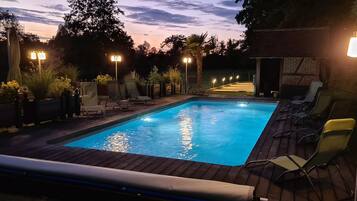 An outdoor swimming pool with lounge chairs and lights, surrounded by plants and a brick structure.