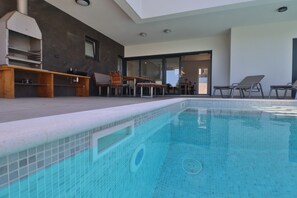 Un espace piscine extérieur moderne, doté d’un barbecue intégré et de coins salon.