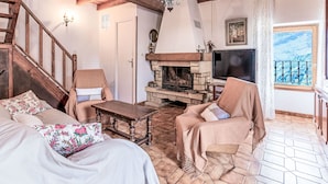 Ein gemütliches Wohnzimmer mit Kamin, Holzbalken, Fernseher und einem Balkon mit Blick.