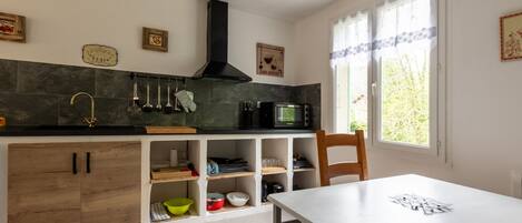 A kitchen with wooden cabinets, a black microwave, and a window with curtains.