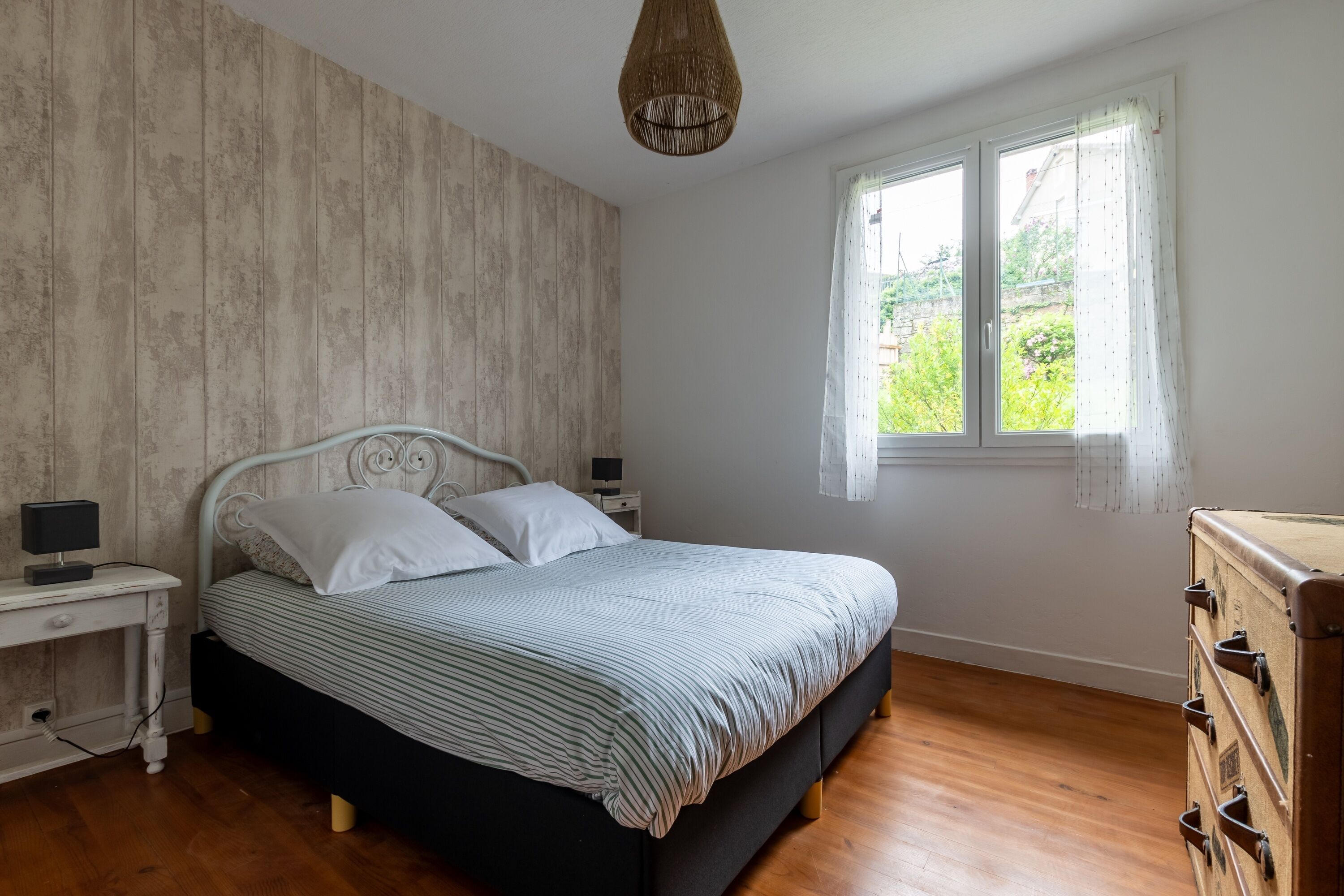 Une chambre à coucher avec un lit, des tables de chevet, une commode et une fenêtre avec des rideaux.