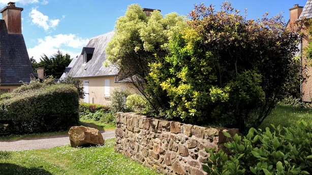 A stone wall with a pathway leading to a house with a sloped roof.