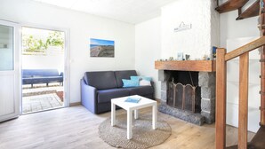 A cozy living room with a sofa, a small table, a fireplace, and a view through a glass door.