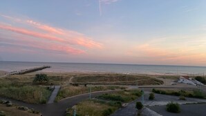 Eine Küstenlandschaft mit einer Promenade, Grünflächen und einem Gebäude in Strandnähe.