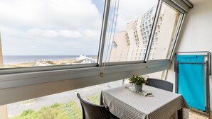 Ein Balkon mit Tisch und Stühlen, einem Blumentopf und Blick auf das Meer und die Gebäude.
