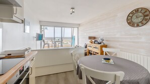 Eine kompakte Küche mit Essbereich, einer großen Uhr an der Wand und Blick durch das Fenster.