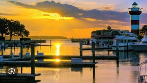 Ein Yachthafen mit vertäuten Booten, ein Leuchtturm und ein Sonnenuntergang über dem Wasser.