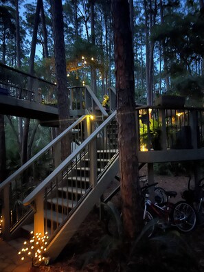 Eine Holztreppe führt zu einer Plattform mit Geländern, umgeben von Bäumen und einem Fahrrad.
