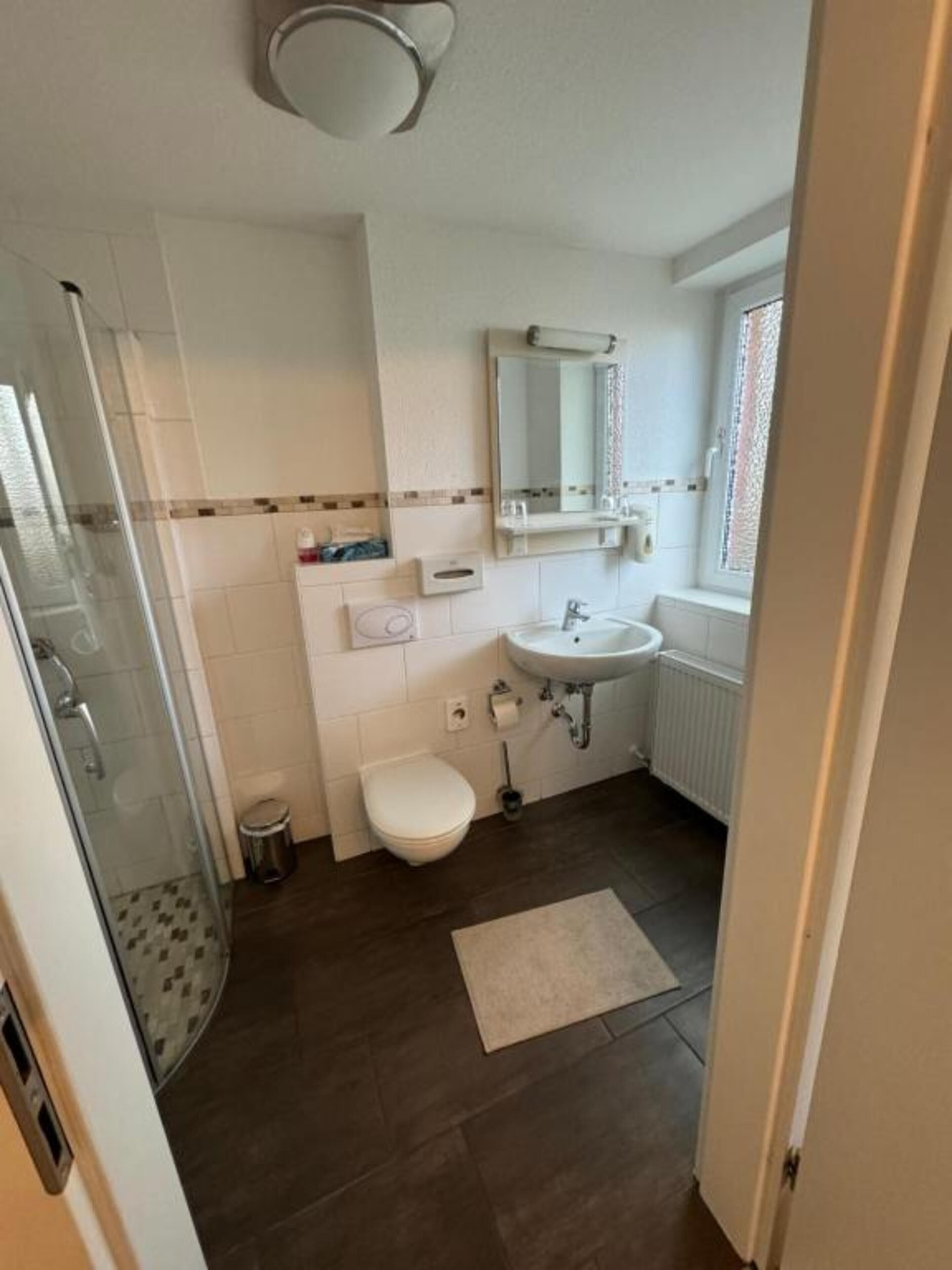A bathroom with a shower, toilet, sink, and a window with blinds.