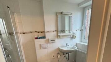 A bathroom with a shower, toilet, sink, and a window with blinds.
