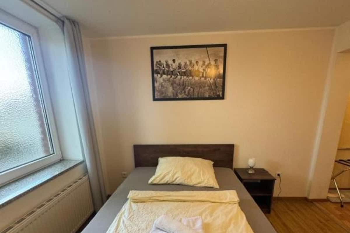 Uma cama de casal com edredom, uma mesa de cabeceira com abajur e um quadro na parede.