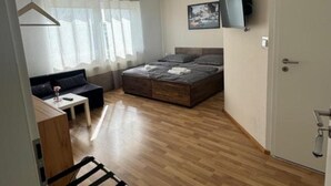 Et lille værelse med seng, lille sofa, skrivebord og fjernsyn.
