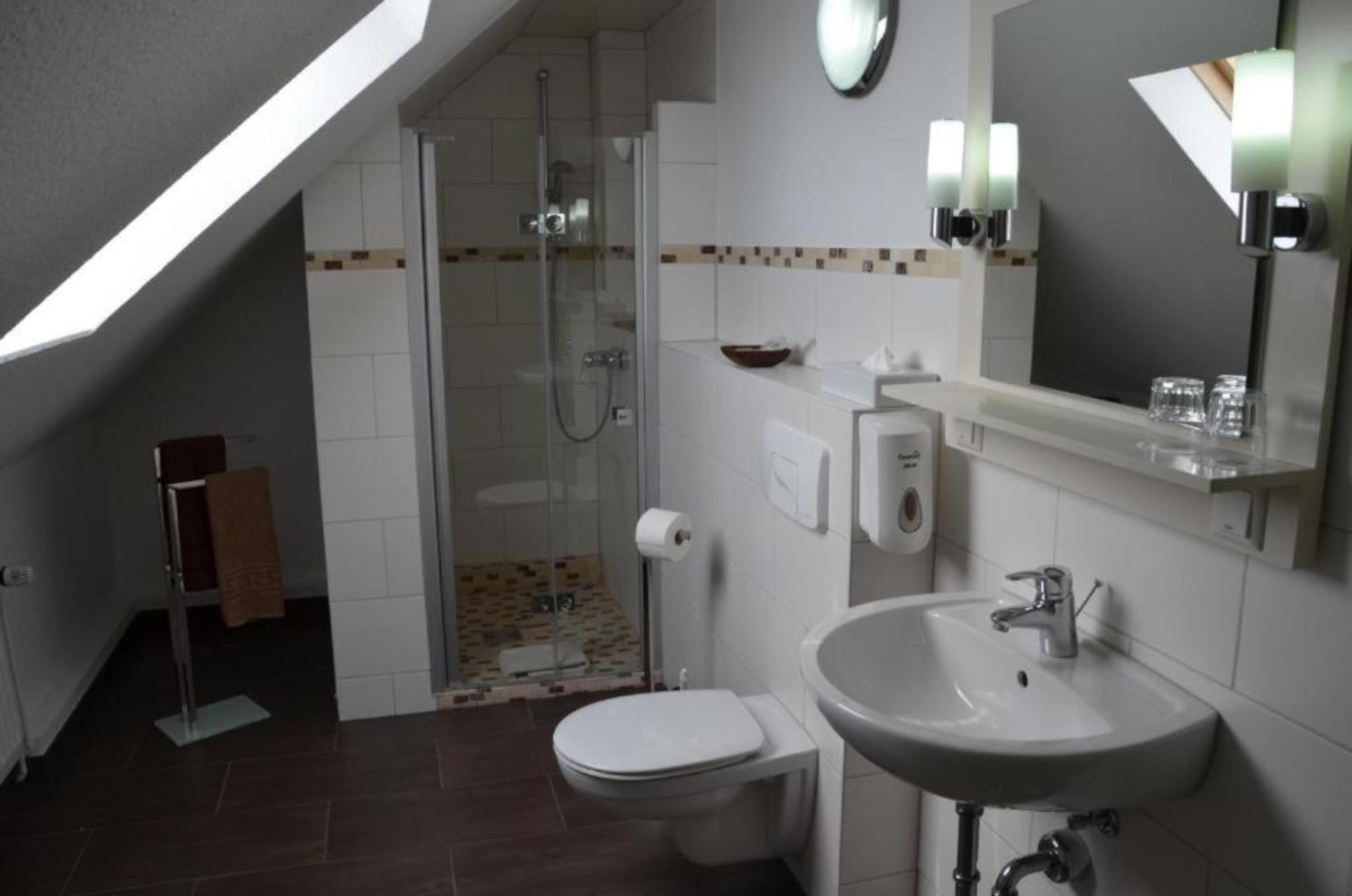 Baño con ducha, inodoro, lavabo y espejo con iluminación.