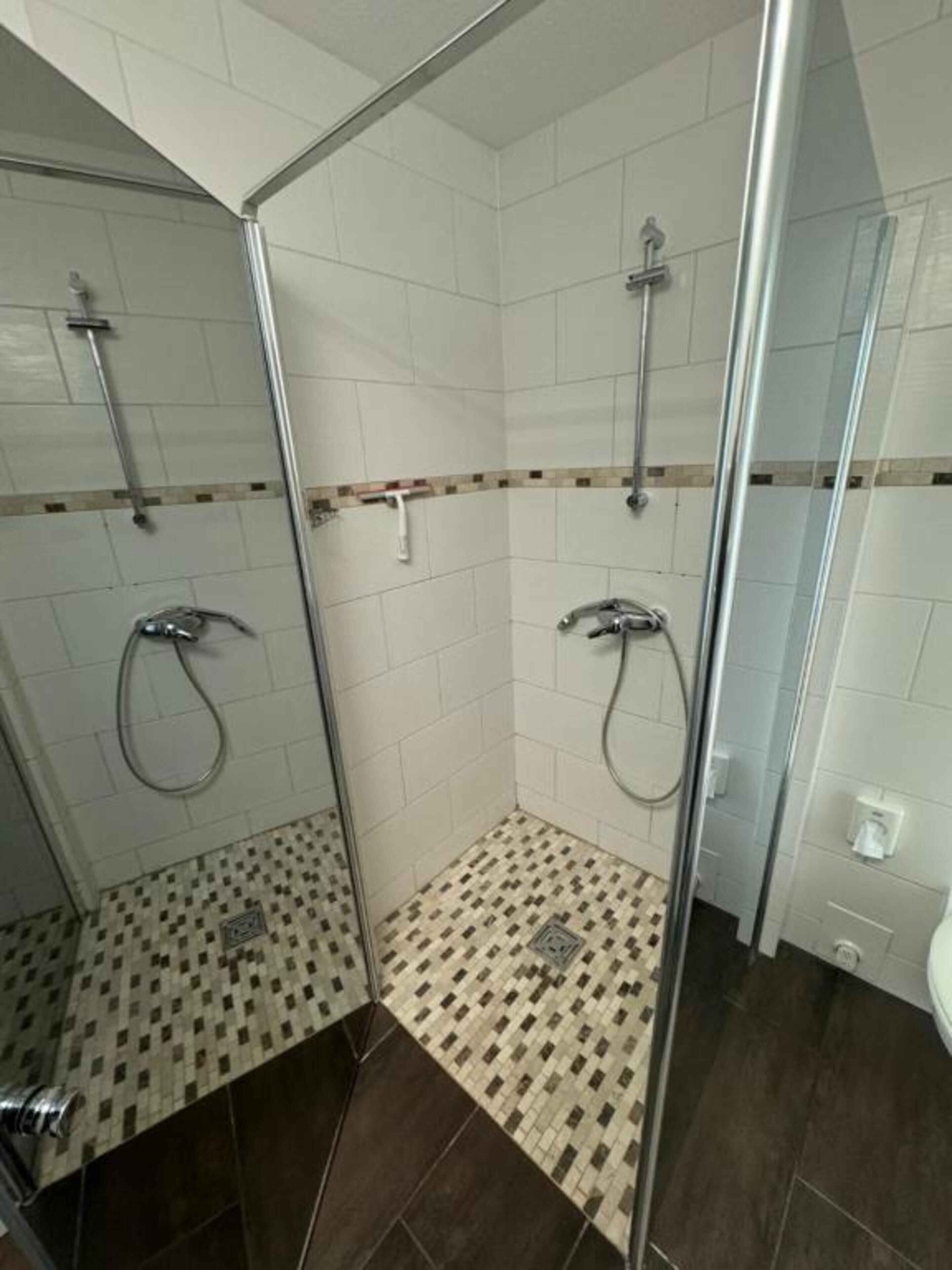 A glass-enclosed shower with a tiled floor and a white wall with a decorative border.