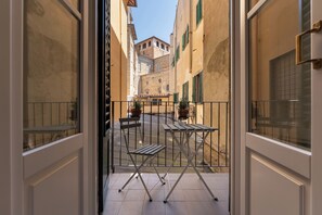 A balcony with a view of a narrow street, a wooden table, a chair, and potted plants. - Appartamento con Camera Tripla in Palazzo Storico (Firenze)