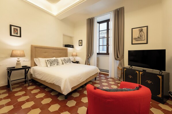 A hotel room with a large bed, a TV, a red chair, and a window with curtains. - Appartamento con Camera Tripla in Palazzo Storico (Firenze)