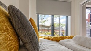 A bed with white bedding and a yellow blanket, pillows in shades of yellow and gray, and a view of a building through a window. - City Centre Deluxe with amazing Garden Terrace - Pass the Keys (Leeds)