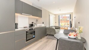 A modern kitchen with grey cabinets, a built-in oven, and a dining area with a grey sofa and table. - City Centre Deluxe with amazing Garden Terrace - Pass the Keys (Leeds)