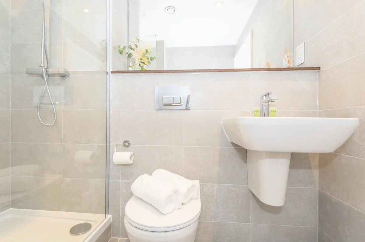 A modern bathroom with a glass shower enclosure, a white toilet, a sink with a mirror above it, and a small shelf with toiletries.