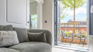 A modern living room with a grey sofa, a cushion with text, and a sliding glass door leading to an outdoor patio with a table and chairs. - City Centre Deluxe with amazing Garden Terrace - Pass the Keys (Leeds)