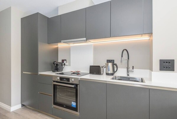 Una cucina moderna con mobili grigi, forno integrato, macchina per caffè, bollitore e tostapane.