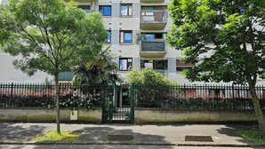 A residential building with multiple balconies, a gated entrance, and surrounding greenery.