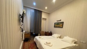 A hotel room with two beds, a desk, a chair, a painting on the wall, and a red patterned carpet. - Hotel The Builder 124 (Tbilisi)