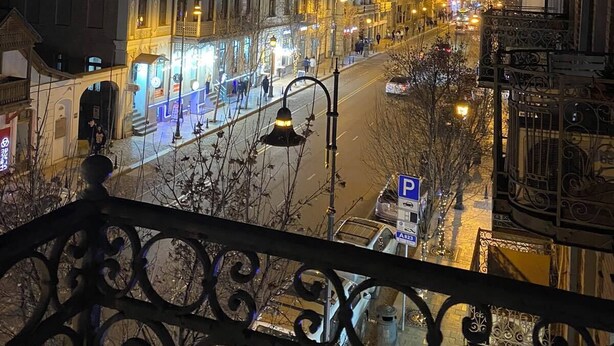 A nighttime view of a city street with illuminated buildings and a clear view of a street sign indicating a parking area. - Hotel The Builder 124 (Tbilisi)