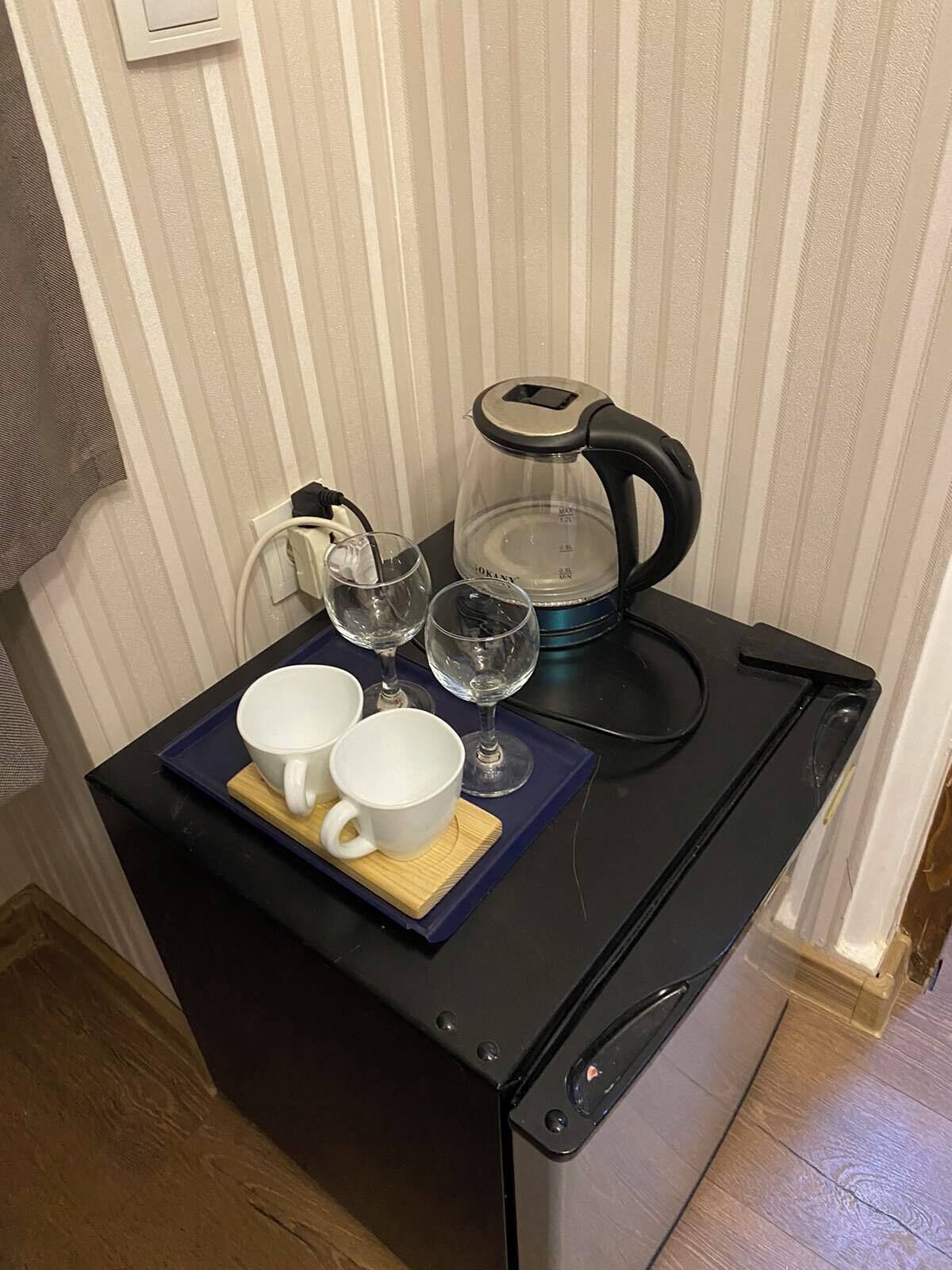 A compact kitchen area with a coffee maker, two white cups, and two wine glasses on a small table.