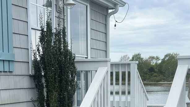 Una casa con fachada blanca, un porche con escalones y una vista de agua al fondo.
