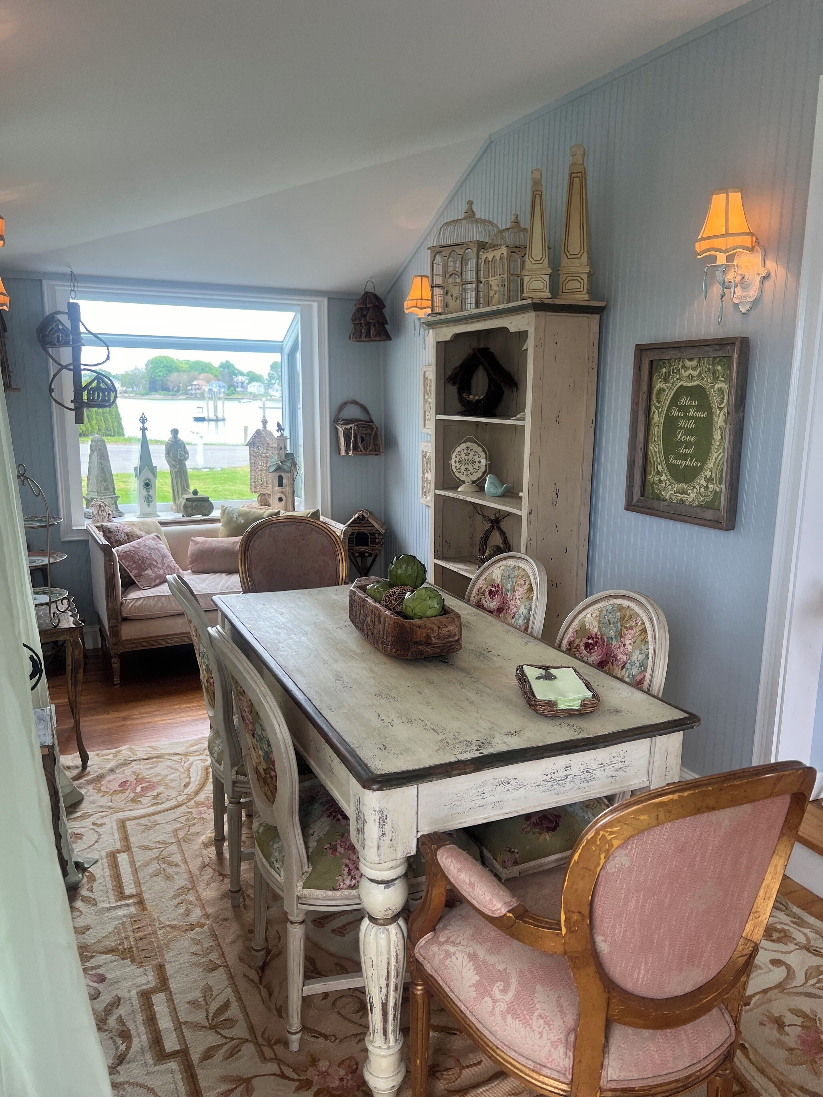 A dining area with a table set for four, surrounded by vintage chairs. A wooden sideboard with decorative items is against the wall.
